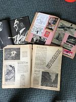 Three open scrapbooks and magazines showing black and white clippings related to World War II including images of Adolf Hitler and aircraft.