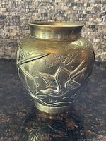 Front side view of a bulbous brass vase showing embossed bird imagery and floral details.