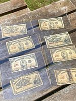 Front side view of all 8 Old Dominion 25 cent bank notes shown laid on wooden boards, showing sepia printed fronts with portraits and denomination.