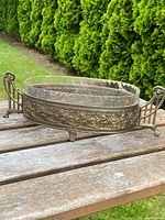 Full image of French silver-plated and glass-lined table centrepiece on wooden surface with greenery background.