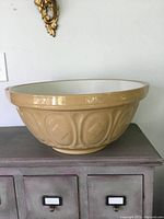 Side view of large beige ceramic mixing bowl with textured exterior pattern placed on a grey cabinet.