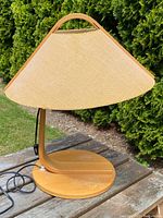 Side view of the mid-century modern bentwood table lamp showing bentwood curved body, round base, and trapezoidal beige fabric shade with a handle-like arch.
