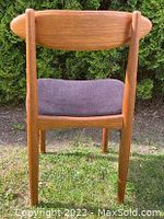 Back view of the teak chair showing curved backrest and cushioned black seat.