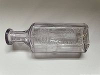 Clear rectangular antique glass medicine bottle lying horizontally to show embossed lettering reading 'Aaronson & Elwin Dispensing Chemist Victoria B.C.'