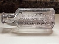 Side view showing embossed text 'CYRUS H. BOWES DISPENSING CHEMIST VICTORIA, B.C.' on clear glass rectangular bottle.