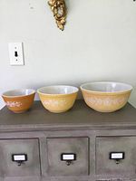 Three yellow Pyrex mixing bowls arranged from small to large showing the graduated sizes and white floral design around the bowls
