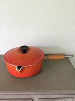 Side view of vintage orange Le Creuset pot with lid and wooden handle, placed on a surface