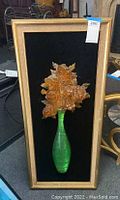 Full view of framed 3D resin art showing green vase and amber roses against black background with gold frame.