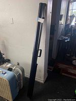 Canvas projection screen contained in slim black metal carrying case standing upright against wall indoors.