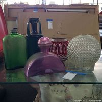 Front view of five assorted crystal and glass items including bottles and decorative pieces on a glass shelf.