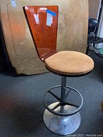 Full view of an orange acrylic back bar stool with round padded seat and metal base with footrest ring.