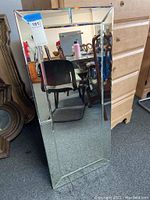 Full front view of tall rectangular beveled edge wall mirror leaning against furniture showing overall shape and design.