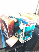 Boxed Conair heated massaging neck rest and other boxed items on black surface, partially opened.