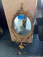Full view of an oval decorative wall mirror with a gold-colored ornate frame showing floral and curved motifs.