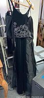 Two black evening gowns hanging on a rack. One has a beaded bodice with silver swirl and floral patterns; the other is plain black satin.