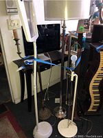 Photo showing six lamps clustered together, including a white magnifying lamp, brass candlestick lamp, brown decorative lamp, stainless steel lamp with beige shade, white lamp with exposed bulb, and a partially visible lamp behind them.