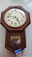 Front view of wooden octagonal-faced wall clock with 'REGULATOR' glass panel on lower part and visible brass pendulum, showing wear and damage.
