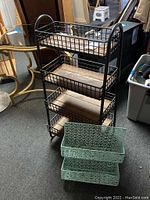 Metal frame kitchen rack with three wooden shelves and two green metal wall racks with decorative patterns in background