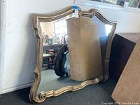 Front view of the large gold-tone wall mirror showing its ornate curved edges and gold finish.