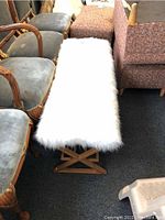 Front angled view of metal bench with white fuzzy seat showing the X-shaped base and surrounding chairs