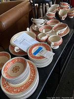 Photo showing various plates, cups, saucers, and serving pieces all decorated in orange and white Medici pattern assembled on table.