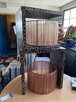 Two wood nesting end tables stacked with two cream sheer fabric lamp shades placed on and beside them in a workshop setting.
