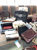 Wide shot of the assortment of purses and handbags laid out on a table including bags in black, beige, brown, and cream colors.
