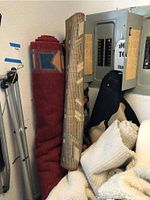 Rolled rugs stacked near electrical panel, showing geometric and woven designs.