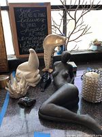 Photo showing multiple sculptures including sea lion, reclining woman, decorative mask, and others on floor in front of window.