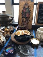 Photo showing a collection of vintage clocks, artwork, brass and silver-tone teapots, ceramic decor, and glass dishes arranged on a windowsill.