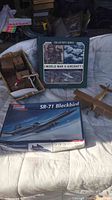 Photo showing the SR-71 Blackbird model kit box, World War II aircraft collector's book, wooden biplane model, and part of the puzzle basket