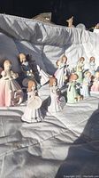Lot of 12 youthful girl figurines arranged on a white background representing various ages and stages of growth.