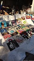 Records laid out on white cloth showing vinyl records and various sleeves including images of Tina Turner and Genesis and multiple record labels