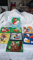 Seven colorful, complete wooden puzzles laid out on a white cloth, including Red Riding Hood, Mickey Mouse, Dumbo, a tiger, and other cartoon characters.