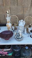 Overview of lot showing angel figurines, 24K gilded Asian ceramic lamp, wooden bowl, small rattan chairs, and candelabras on table