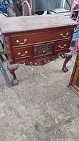 Full front view of the four-drawer solid wood cabinet showing brass handles and decorative carvings on drawer fronts and apron. Cabinet stands on claw feet.