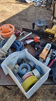 Overview photo of the lot showing power tools, hand tools, tape rolls, hoses, extension cords on a table outdoors.