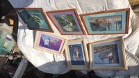 Seven framed Disney stencils laid on white fabric outdoors, depicting various scenes from Disney movies.