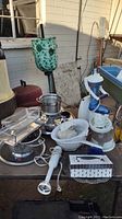 Wide view of kitchen lot showing Arctic Twister juicer, Black & Decker juicer, pet plates, drainers, immersion blender and fondue set on outdoor table.
