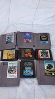 Nine game cartridges: five Nintendo NES gray cartridges, three Sega Genesis black cartridges, one Atari black cartridge. Labels visible with various game titles.