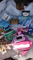 Full view of all toys, books, and coloring items including new Crayola box, My Little Pony, Ingenious Machines kit, pink handheld game device, and blue toy animal truck.