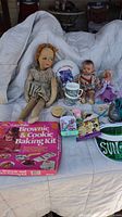 Photo showing two vintage dolls, Easy-Bake Oven Brownie & Cookie Baking Kit box, a cartoon-themed cup, Frisbee, and some collectible toys.