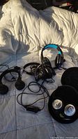 Photo showing multiple wired headphones including Skullcandy and JBL brands in used condition lying on white bedding.