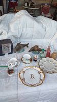 Wide shot of all items arranged on white quilt: 3 teacups with saucers including boxed Spode Ansley, 3 perfume bottles, 2 ceramic fish, 2 ceramic ducks, 2 plates