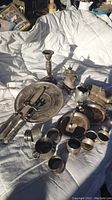 Wide view showing multiple sterling and silver plated items including candlestick, trays, napkin rings, and drinking cups arranged on a white blanket.