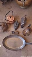 Photo of three antique irons, three copper pots including teapots and kettle, cast iron pan and small metal kitchen tool.