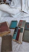 Photo showing lot of 8 vintage books on a white cloth background, various worn covers and colors visible