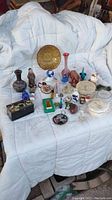 Overview of vintage mini trinkets arranged on white fabric including glass perfume bottles, figurines, trinket boxes, and decorative plates