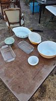 Photo showing full assortment of bowls and glass loaf pans on table outdoors with vintage chair in background.