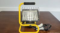 Front view of the 500 watt portable work light showing yellow tubular frame, protective metal grille, and reflective interior housing.